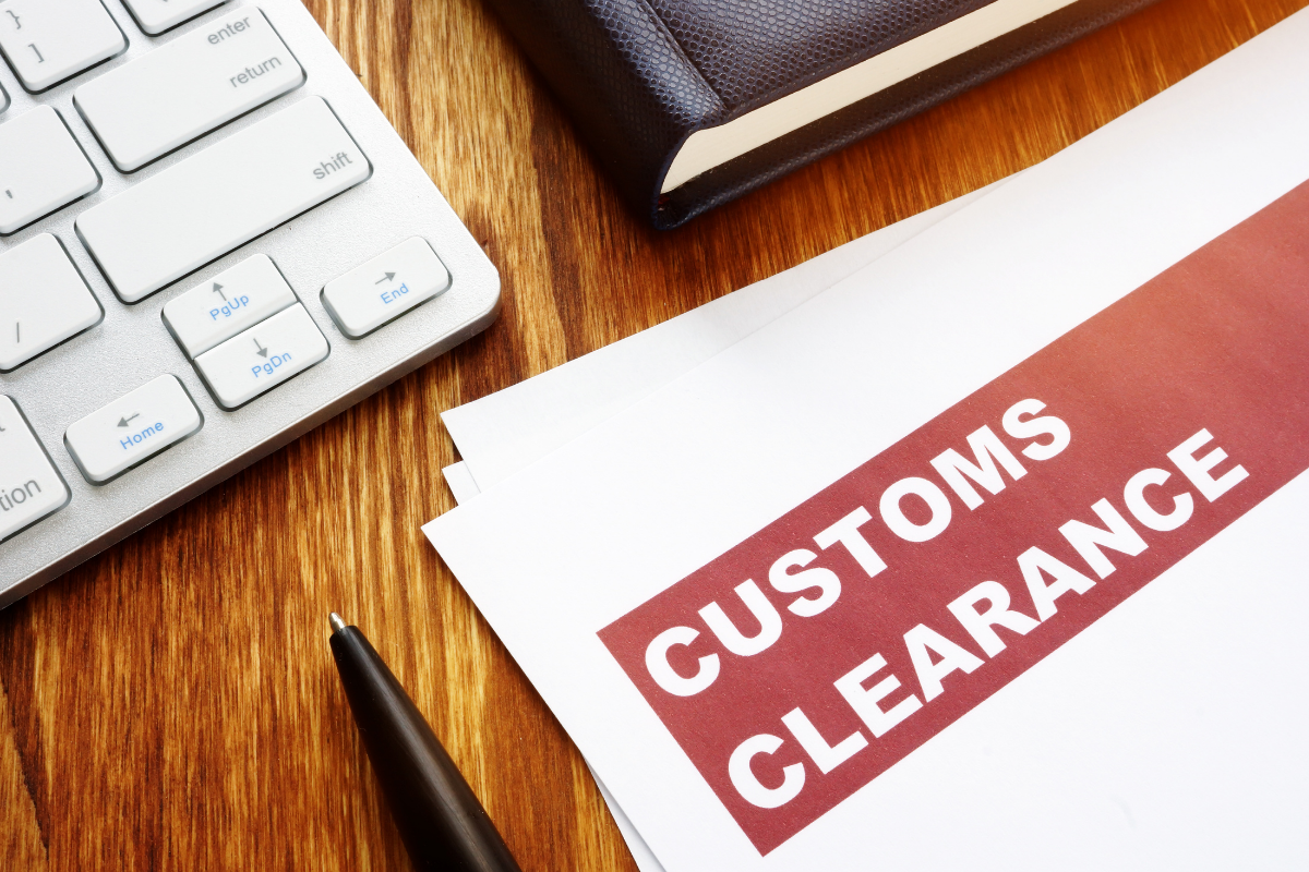 Desk with keyboard, pen, notebook, and document with "customs clearance" highlighted in red